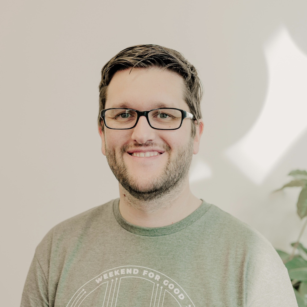 A headshot of Laurence Blackledge. Laurence is taller than average, standard-looking white man with brown hair and stubble. He is against a pale background, smiling lopsidedly, and looks late thirties.