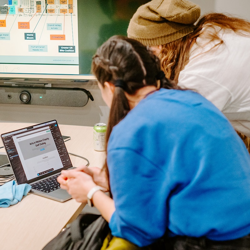 Two volunteers hover over a laptop, working on a website design