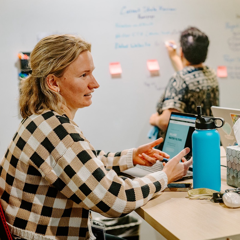 A project team discusses their work and writes on a whiteboard